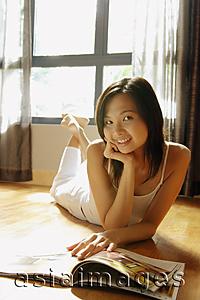 Asia Images Group - Young woman lying on floor with magazine, looking at camera