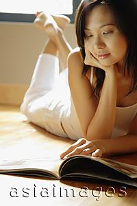 Asia Images Group - Young woman lying on floor reading magazine.