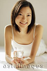 Asia Images Group - Young woman lying on front, holding glass of water