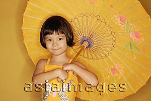Asia Images Group - Young girl standing against yellow background, holding umbrella