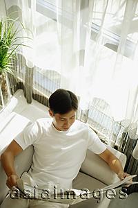 Asia Images Group - Young man reading newspaper, high angle view
