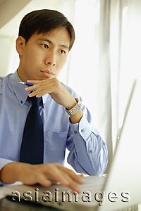 Asia Images Group - Male executive using laptop, hand on chin