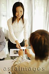 Asia Images Group - Young female executive giving her business card to male executive