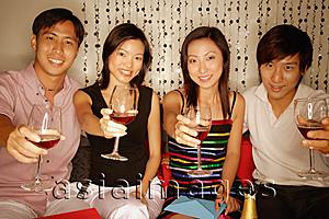 Asia Images Group - Couples sitting down raising wine glasses, looking at camera
