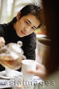 Asia Images Group - Young man pouring tea for young woman in front of him.