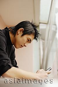 Asia Images Group - Young man using mobile phone, leaning on railing