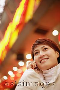 Asia Images Group - Young woman using mobile phone, looking up