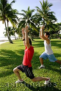 Asia Images Group -  Men doing stretching exercises in park, arms raised upward