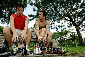 Asia Images Group - Two men on park bench, putting on roller blades, side by side