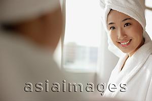 Asia Images Group -  Young woman looking at mirror, towel wrapped around her head