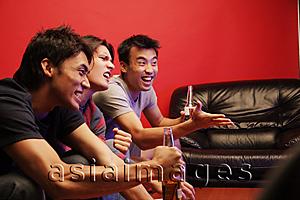 Asia Images Group - Young men holding beer bottles, watching TV
