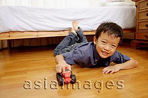 Asia Images Group - Young boy lying on floor with toy car, looking at camera