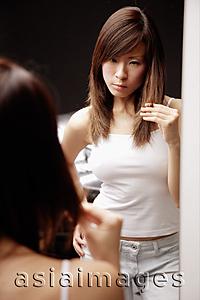 Asia Images Group - Young woman looking at mirror, touching her hair, frowning