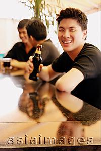 Asia Images Group - Young man at bar counter with beer bottle, smiling at camera