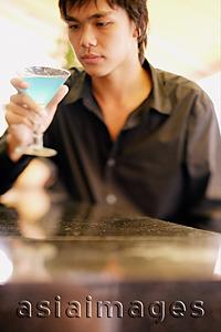 Asia Images Group - Young man at bar counter holding and looking at cocktail glass