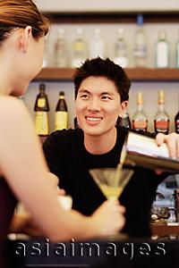 Asia Images Group - Man holding cocktail mixer, pouring drink for woman in front of him