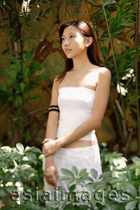 Asia Images Group - Young woman standing and looking away, plants around her