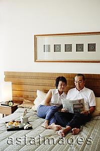 Asia Images Group - Older couple lying on bed, reading newspaper