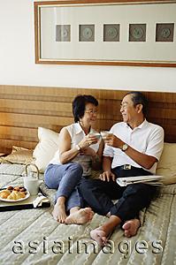 Asia Images Group - Older couple lying on bed, toasting with tea
