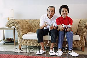 Asia Images Group - Mature couple sitting on sofa playing video games