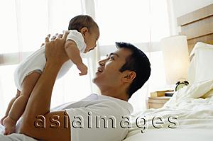 Asia Images Group - Father carrying baby daughter, lying on bed