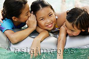 Asia Images Group - Three girls at edge of pool, one whispering to the girl next to her
