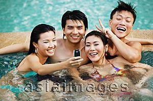 Asia Images Group - Couples in swimming pool, looking at mobile phone