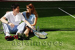 Asia Images Group - Couple sitting down on tennis court, looking at each other