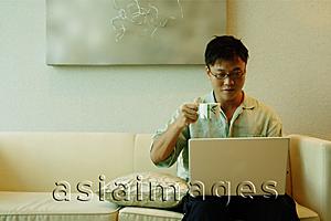 Asia Images Group - Man using laptop and holding cup