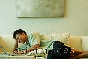Asia Images Group - Man lying on sofa, using laptop