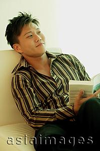 Asia Images Group - Man sitting, holding book, looking away
