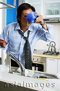 Asia Images Group - Man in kitchen, drinking from bowl