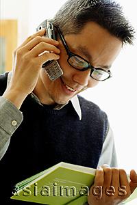 Asia Images Group - Man looking at book and using mobile phone