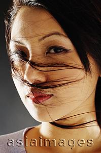 Asia Images Group - Young woman looking at camera, hair blown across her face