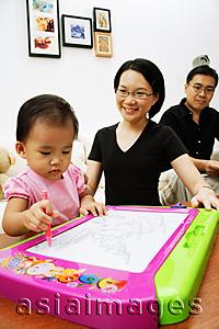 Asia Images Group - Young girl drawing on magnetic block, parents watching her