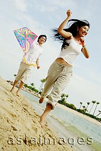 Asia Images Group - Couple flying kite along beach, woman running in front of man