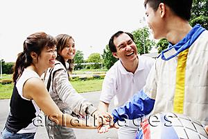 Asia Images Group -  Family of four standing in a circle, putting hands together