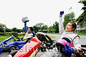 Asia Images Group - Young man and woman in go-carts, hands outstretched, smiling, looking away