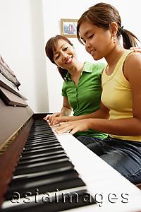 Asia Images Group - Mother and daughter sitting side by side in front of piano, mother with hand on daughter's shoulder