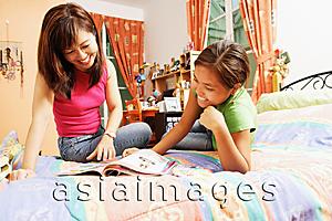 Asia Images Group - Mother with daughter, in bedroom, looking at magazine