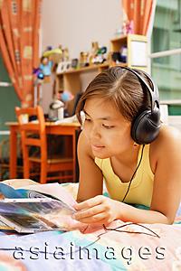 Asia Images Group - Young woman wearing headphones, looking at books