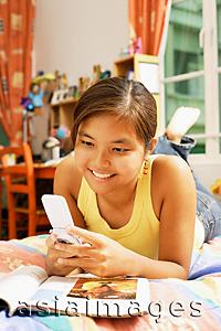 Asia Images Group - Young woman, lying on bed looking at mobile phone