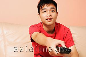 Asia Images Group - Teenage boy sitting on sofa, holding remote control forward