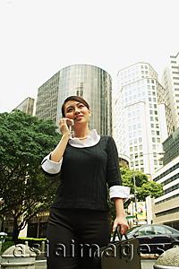 Asia Images Group - Business woman using mobile phone, low angle view, buildings in the background