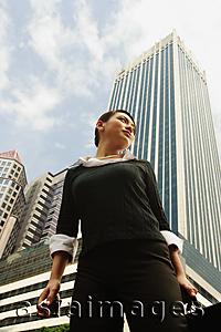 Asia Images Group - Business woman standing, looking away, buildings in the background