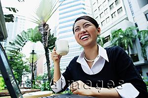 Asia Images Group - Business woman with laptop, holding coffee cup, smiling