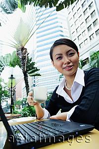 Asia Images Group - Business woman with laptop, holding coffee cup, smiling at camera