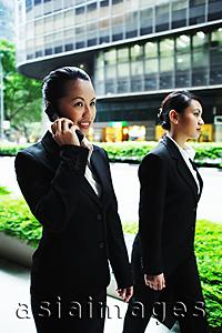 Asia Images Group - Business women walking side by side, one on the phone