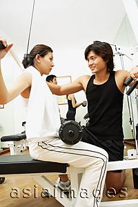 Asia Images Group - Couple working out in gym, woman lifting weights, man helping her