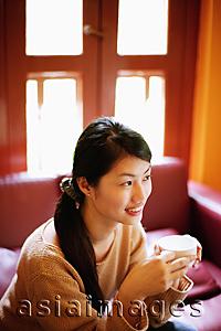 Asia Images Group - Young woman sitting, holding cup, looking away